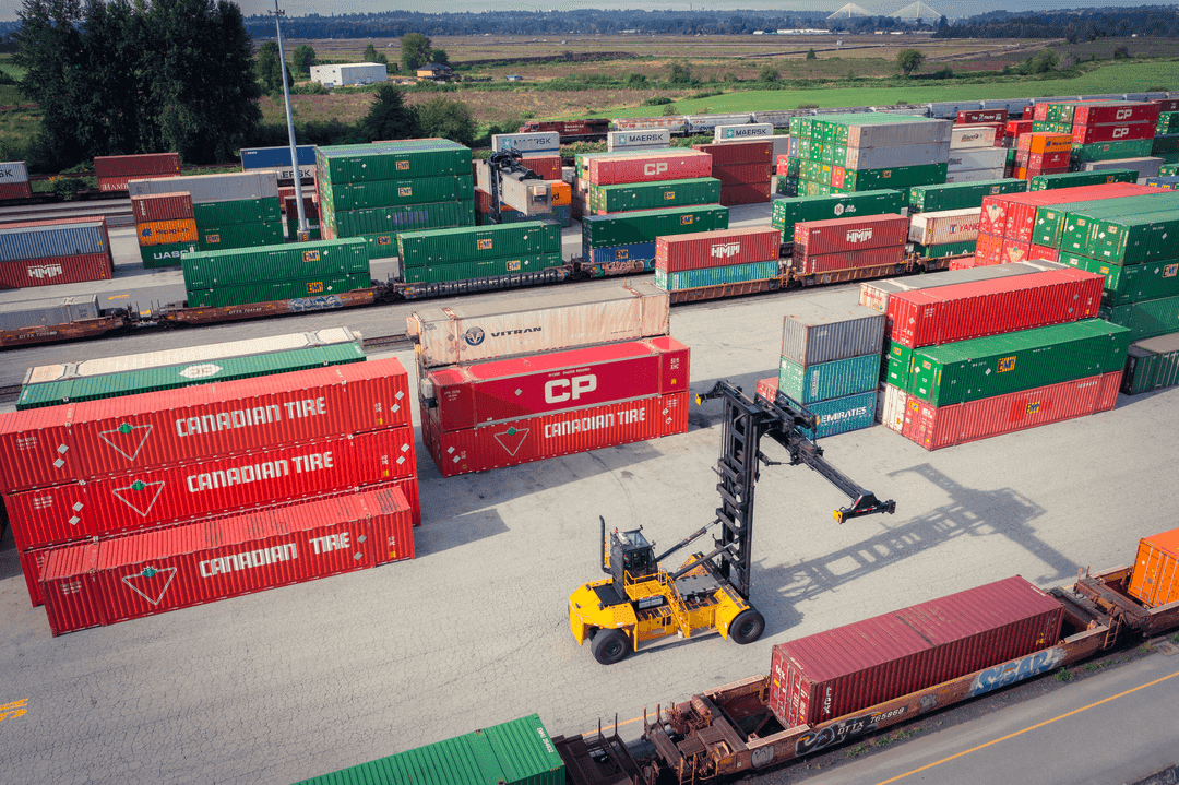 CN and CP intermodal containers stacked at a Calgary rail yard with a reach stacker moving a container between rows