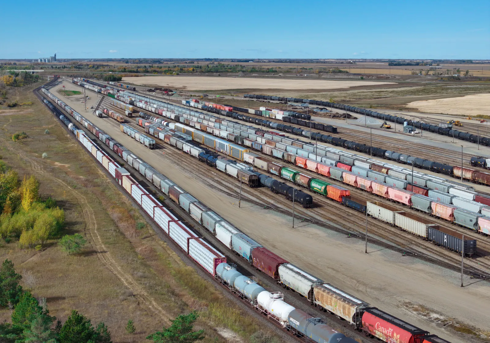 Aerial view of CN's Chappell Yard rail classification yard in Saskatoon, Saskatchewan — long rows of freight and grain hopper cars on parallel tracks beside farmland